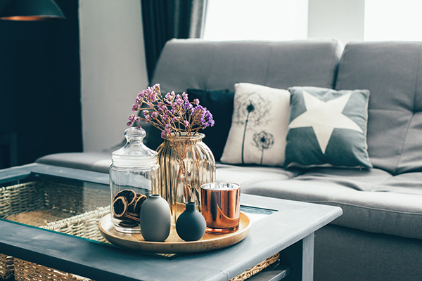 Ein Wohnzimmertisch mit Dekoartikeln steht vor einem Sofa mit Wohnkissen.